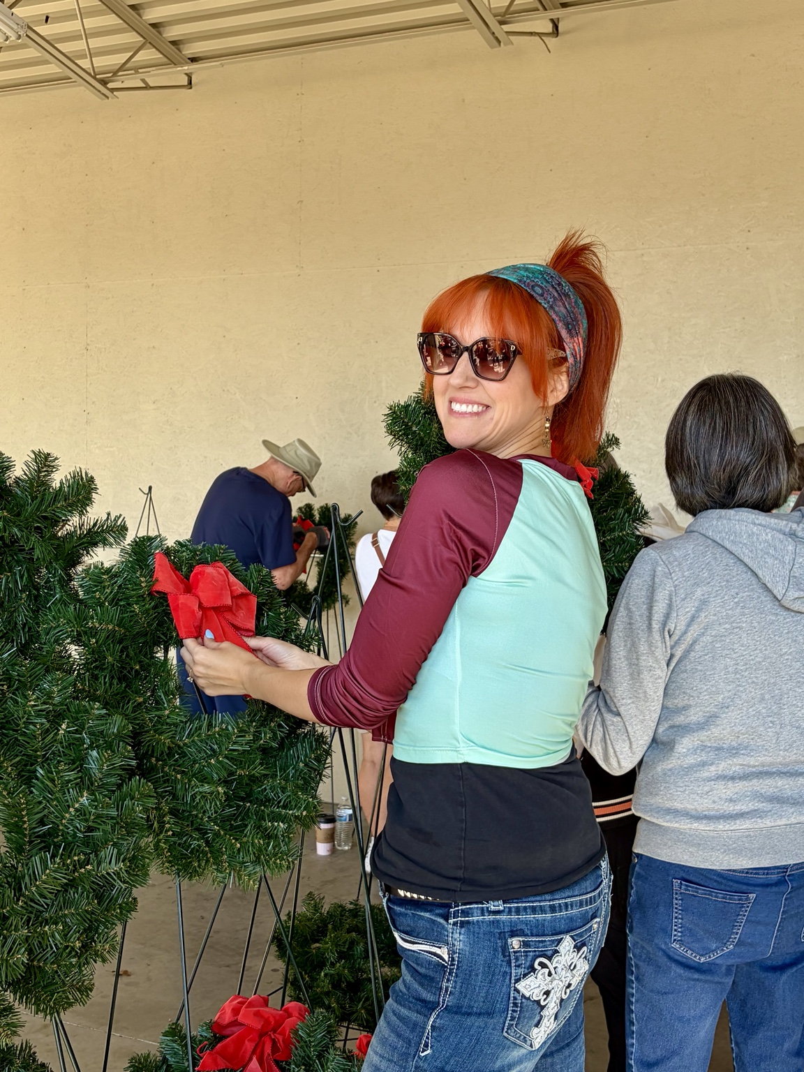 A volunteer adding a red bow to a reusable wreath alongside other volunteers.